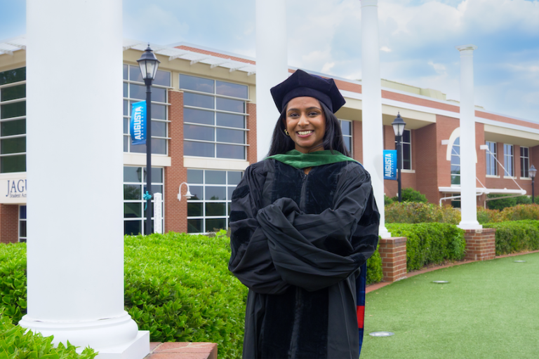 A graduating female student is smiling with four white pillars in the background