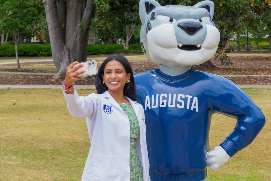 A female graduate student in a lab coat taking a selfie with the Augustus statue 