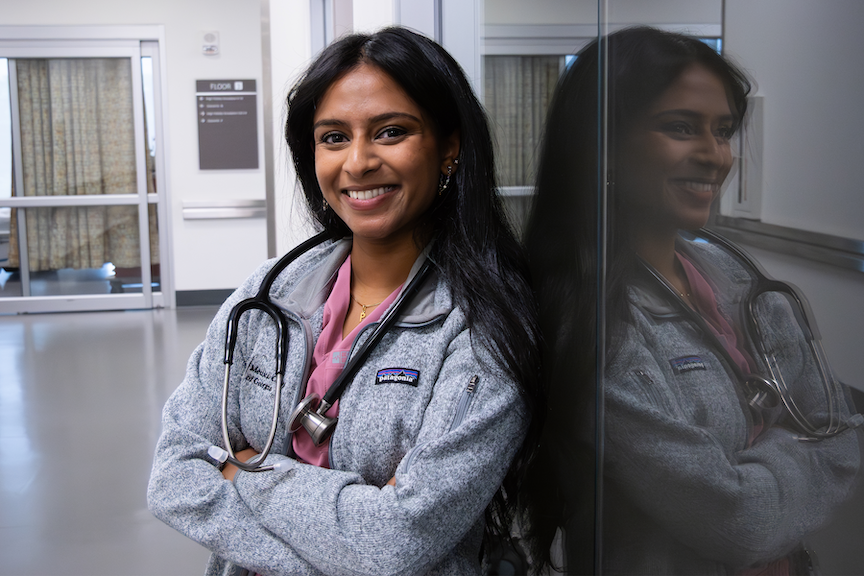 A female graduate student is posed with her arms crossed and smiling against a glass wall