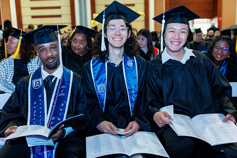 three male students in graduation robes sitting together 