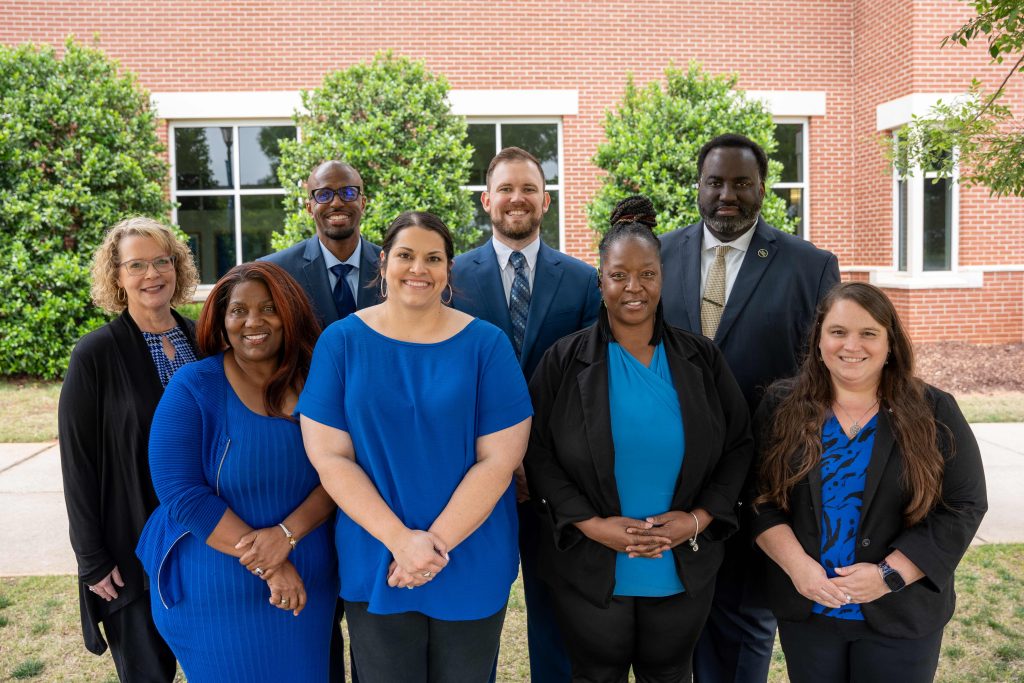 Five women and three men in business professional wear smile for a photo while standing outdoors.