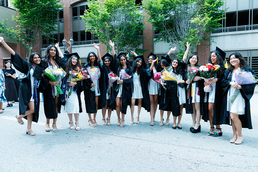 group of female students in white dresses and graduation robes celebrating 