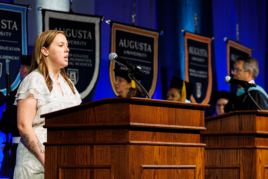 female student wearing a white dress sings at a podium 