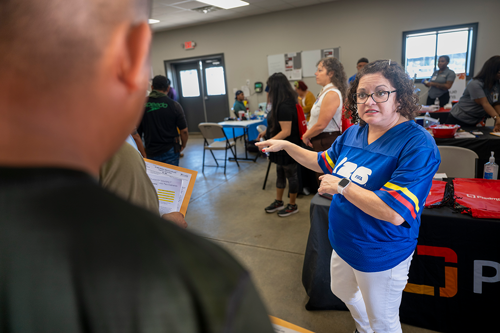 A woman wearing a soccer jersey speaks to men in line at a health fair.