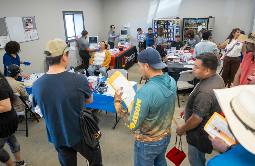 A group of men holding folders wait in line at a health fair to receive heath screenings.