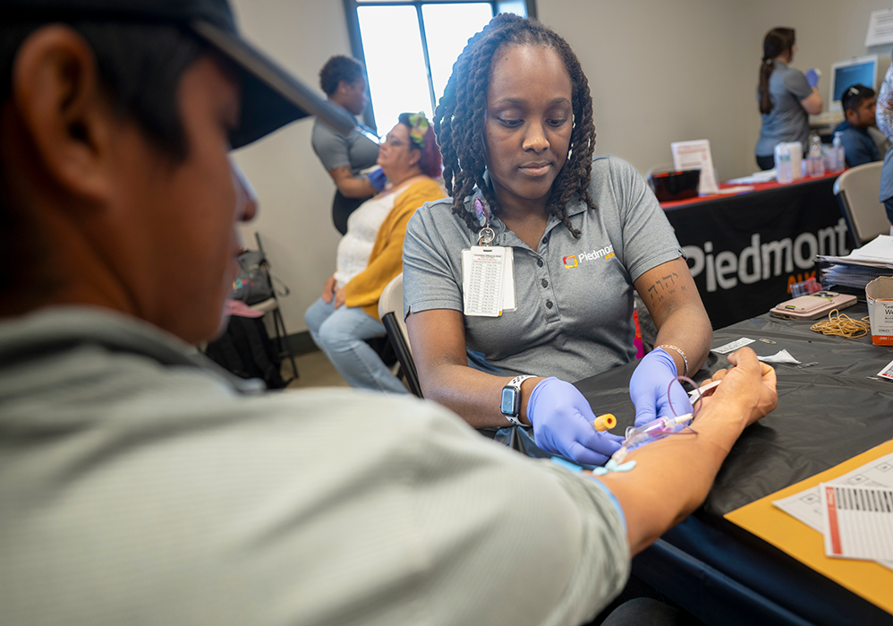 A woman wearing gloves draws blood from a man.