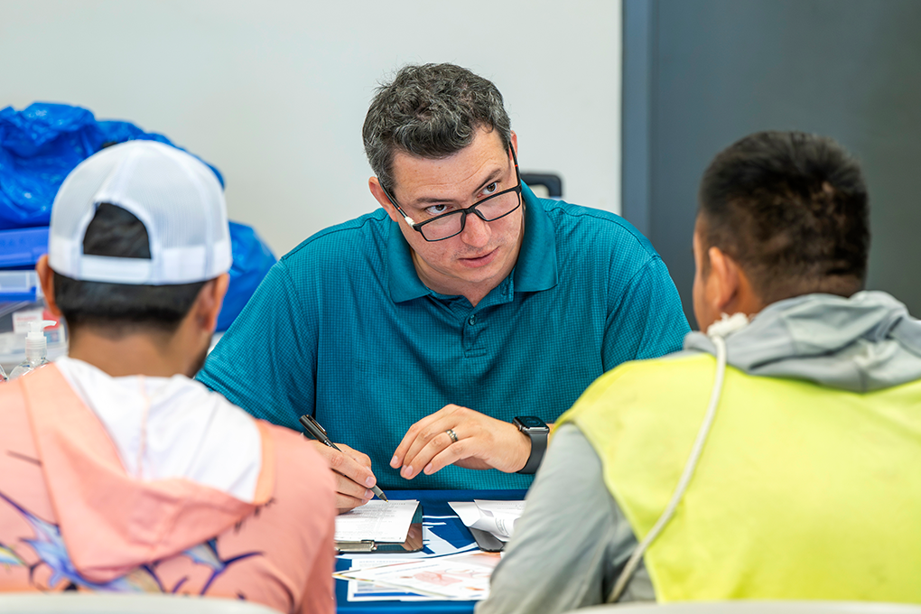 Two men sit across from another man wearing glasses and have a discussion.