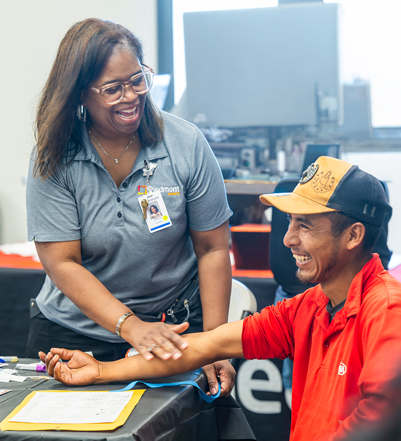 A woman and a man smile and laugh while she performs a health screening on him.