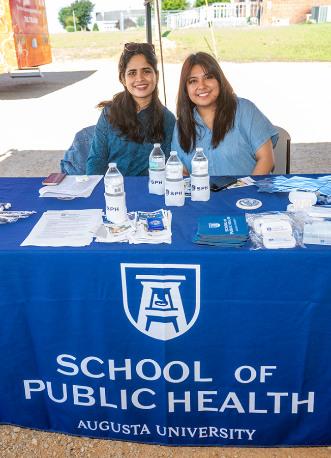 Two women sit behind an Augusta University School of Public Health table at a health fair.