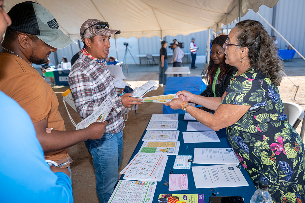 Two women standing behind a table at a health fair hand a man a sheet of paper.
