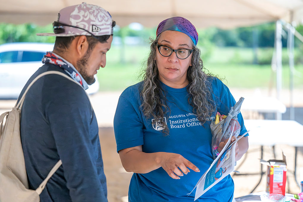 A woman wearing glasses and a bandana on her head speaks to a man and points at something on a sheet of paper.