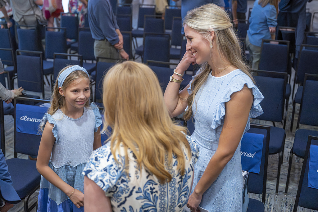 A woman smiles as she looks at her daughter talk to another woman