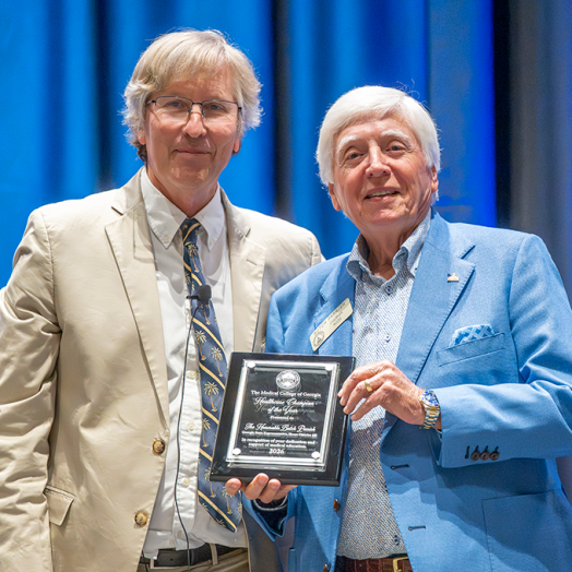 Two men in business dress, one holding a plaque.