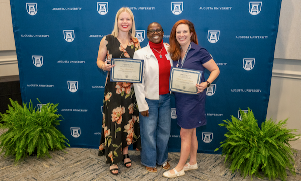 Three women stand with certificates