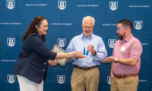 A woman hands an award to two men
