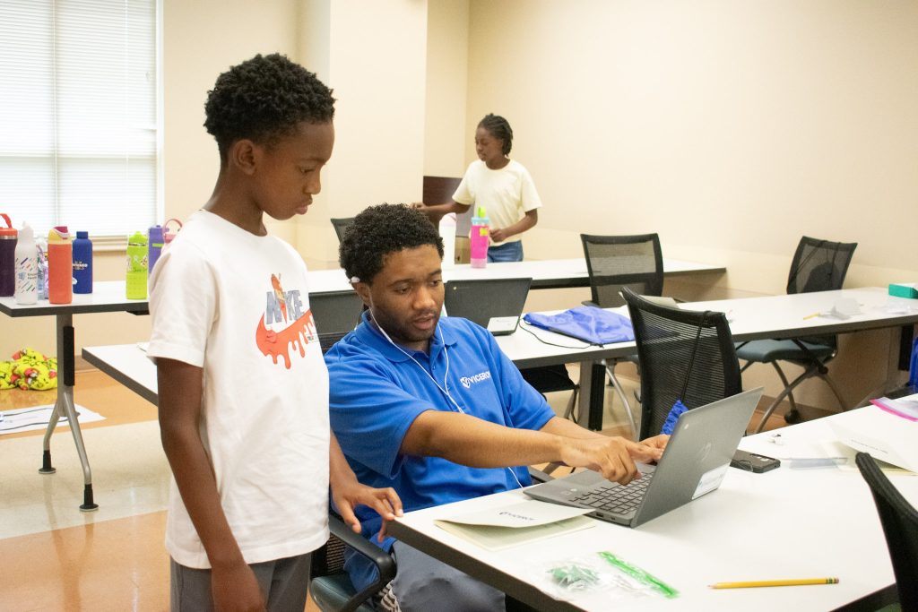 A man working on a computer helping a boy at a table.