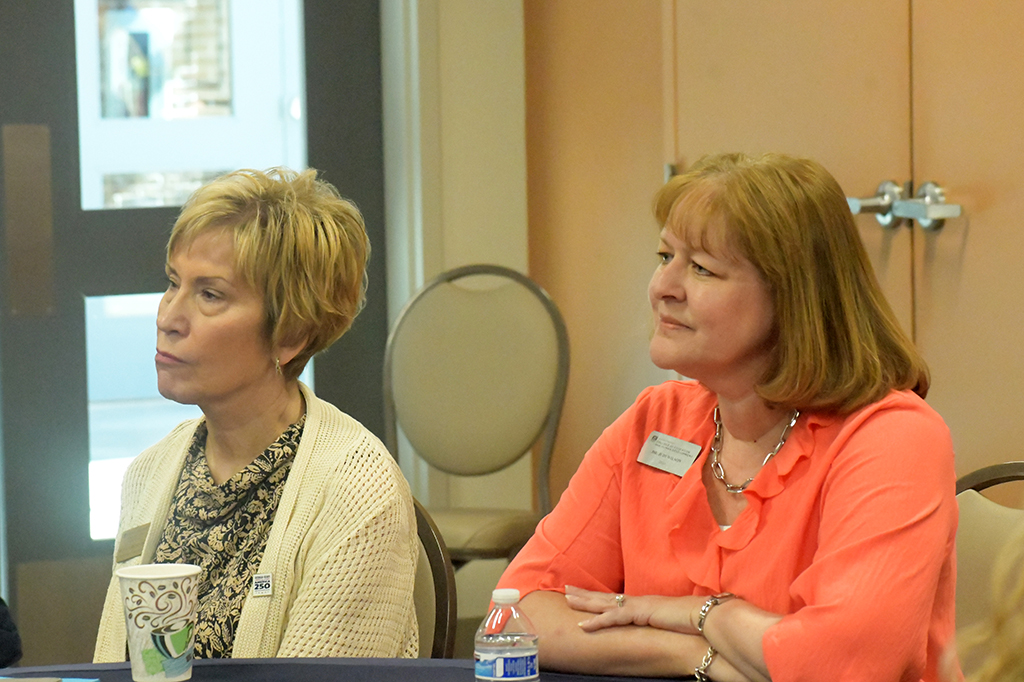Two women sitting at a table listening to a speaker