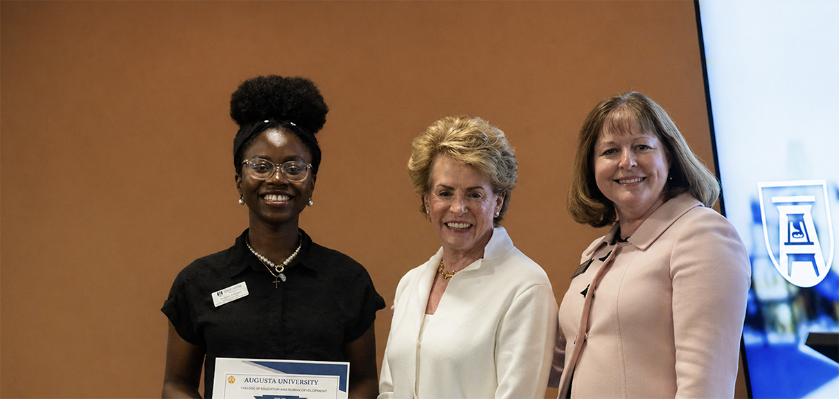A female student holds a certificate while two women stand next to her.