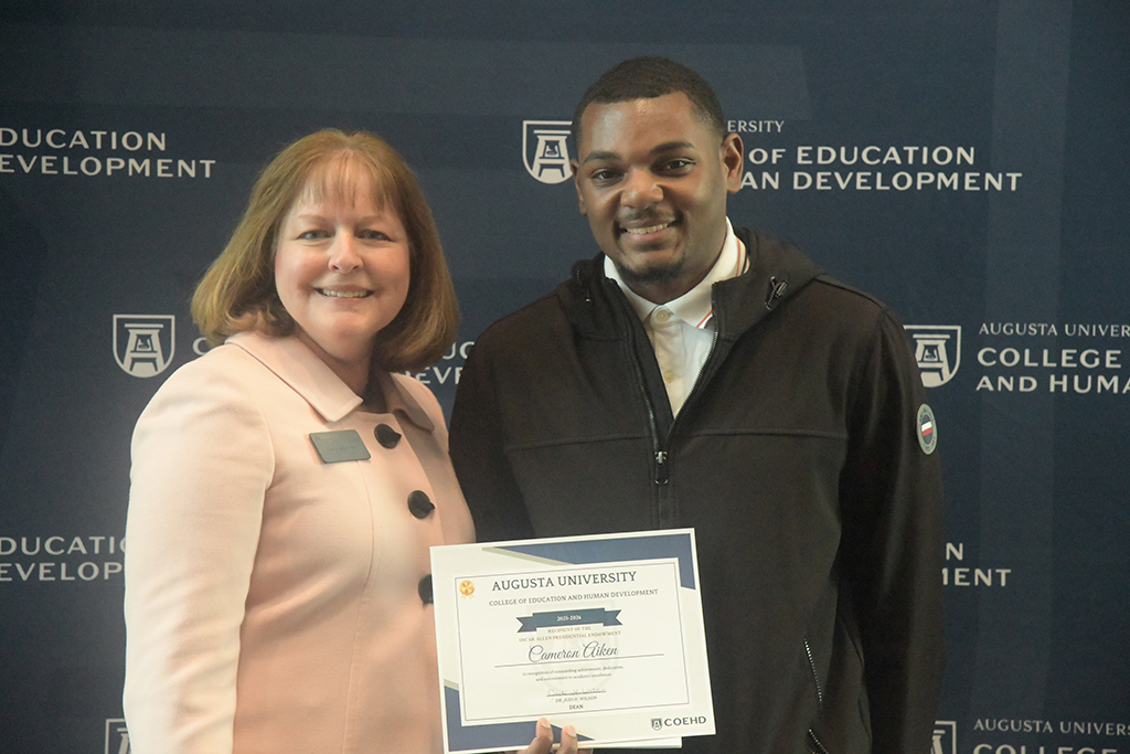 A male student holds a certificate next to a woman