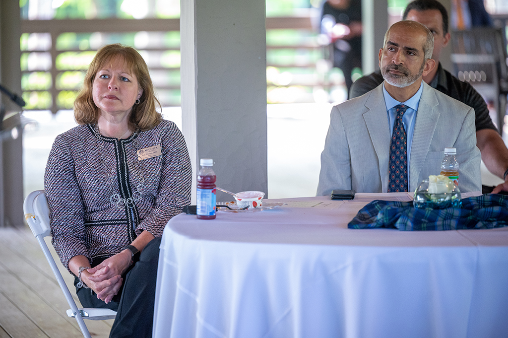 A woman sits at table listening to a speaker with a man sitting next to her