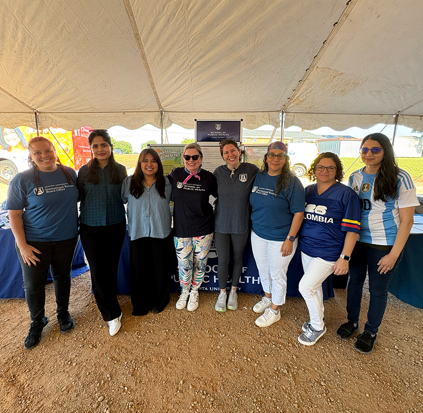A group of women at a health fair stand and smile at the camera.