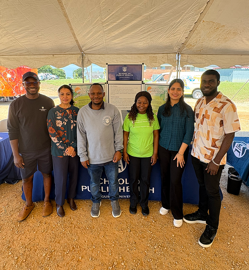 A group of PhD and master's students standing together under a tent at a health fair smiling at the camera.