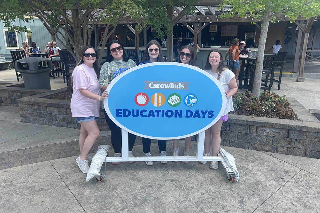 Group of people pose for photo in front of sign outdoors