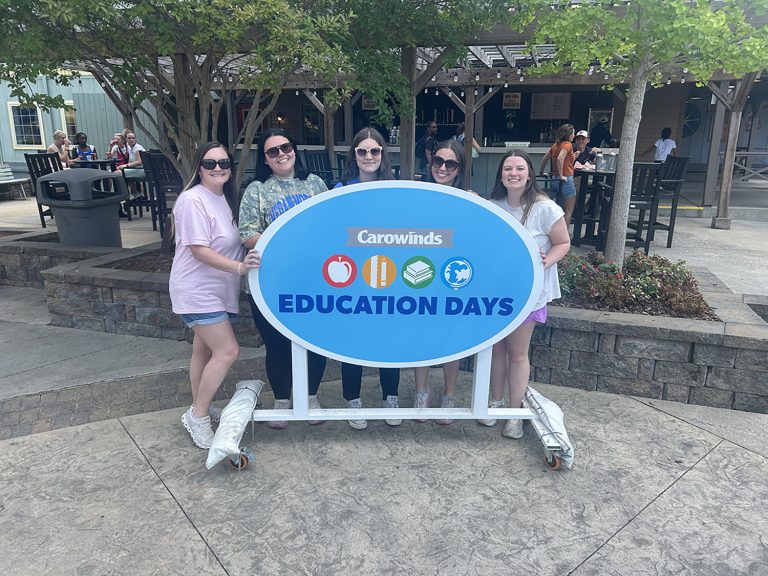 Group of people pose for photo in front of sign outdoors