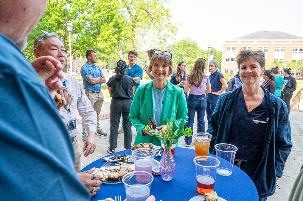 Men and women gathered standing around a small table with food and drinks.