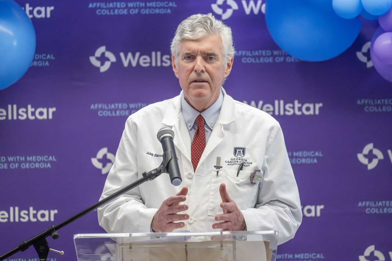 In this photo, you see a man standing in front of a crowd and speaking behind a lectern.