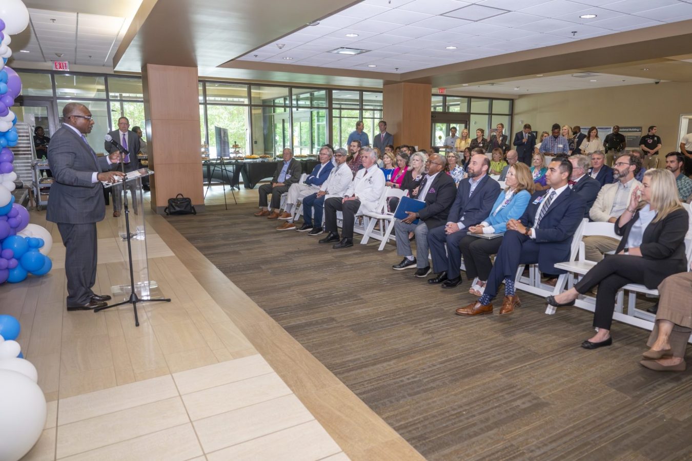 In this photo, you see a man standing in front of a crowd and speaking behind a lectern.