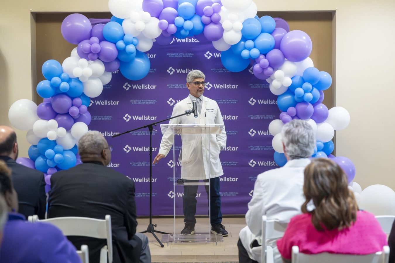In this photo, you see a man standing in front of a crowd and speaking behind a lectern.