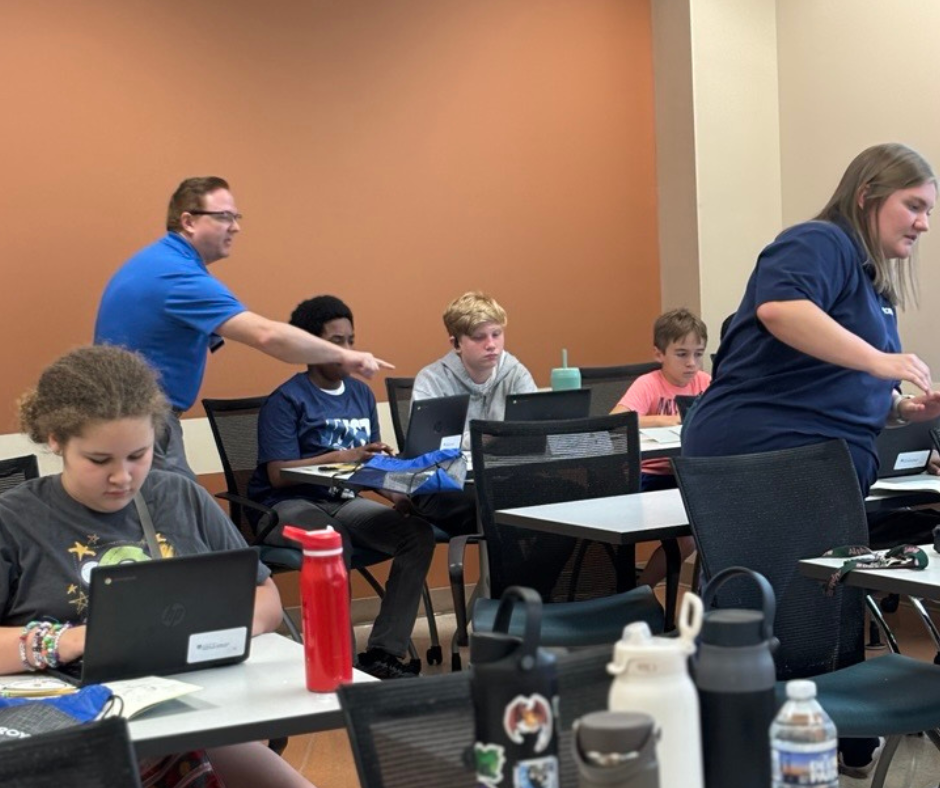 Instructors interact with campers while showing them how to code projects.