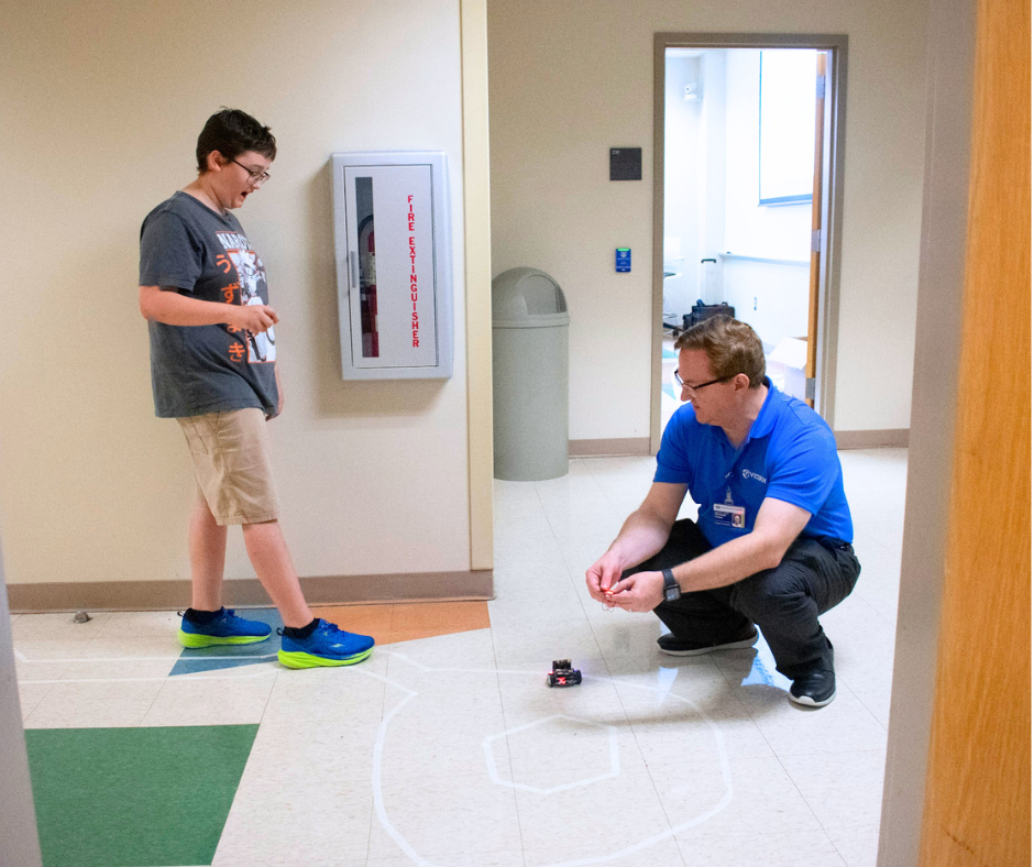 Student interacts with an instructor while testing a Micro:bit Cutebot on a track.