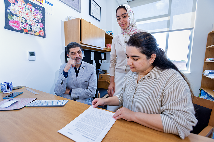 Two female scientists and a male scientist review a print out of an article they wrote.