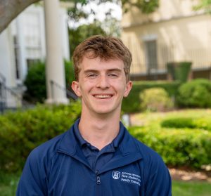 A college-aged man smiling for a photo while standing outside.