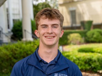 A college-aged man smiling for a photo while standing outside.