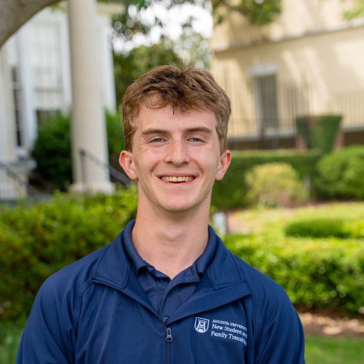 A college-aged man smiling for a photo while standing outside.
