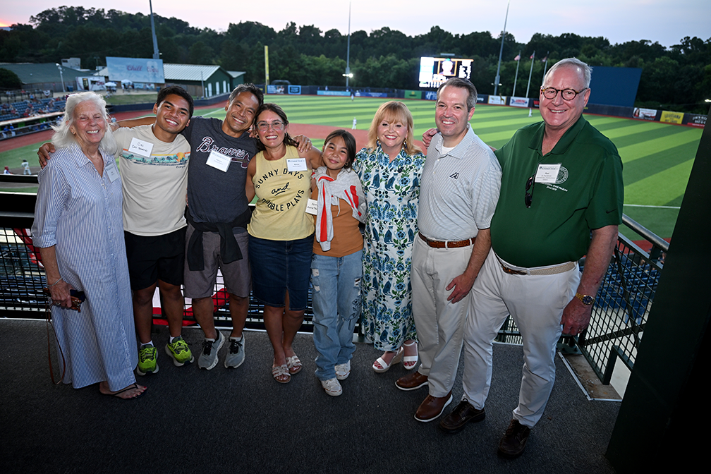 Men in women linked in arms with baseball field behind them
