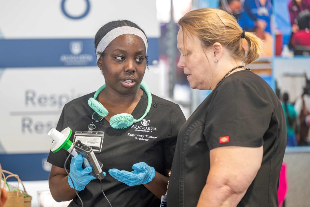 Two women in scrubs talk together, they are looking at some equipment one of them is holding in her hands.