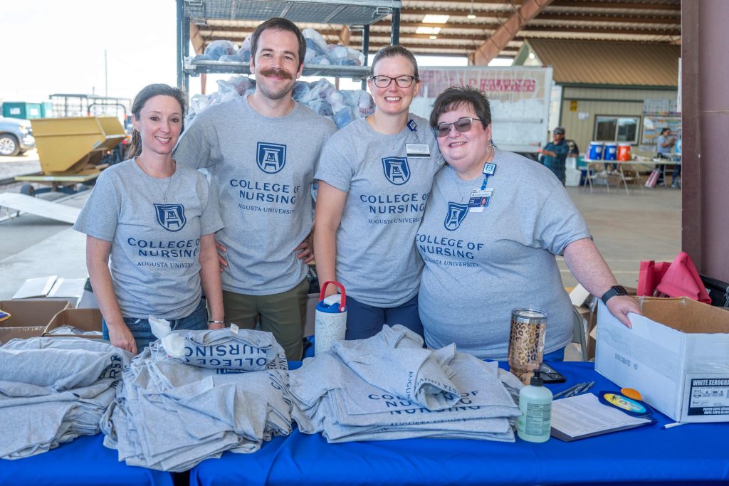 4 people in matching t-shirts pose behind a table covered in t-shirts. They are all smiling at the camera.