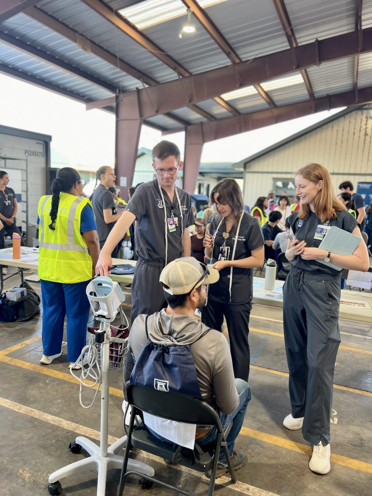 MSN students in scrubs gather around a health fair participant to check his blood pressure