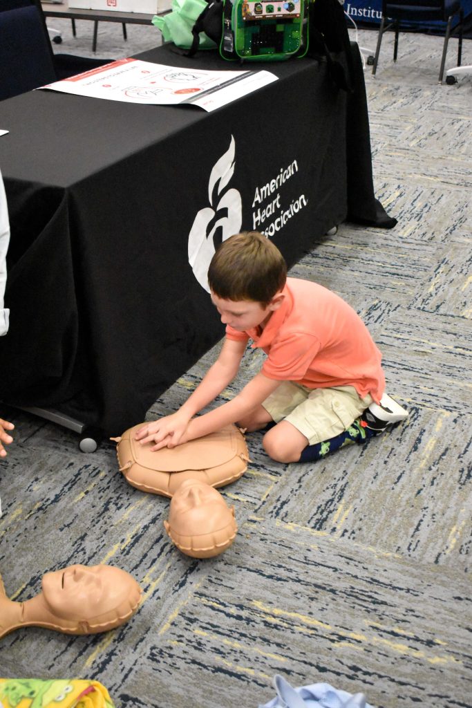 A child sits on the floor and practices CPR on a dummy torso.