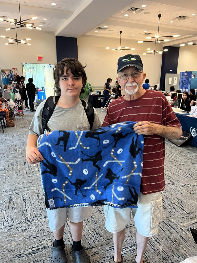 A young man and an older man stand together holding up a hockey themed blanket.