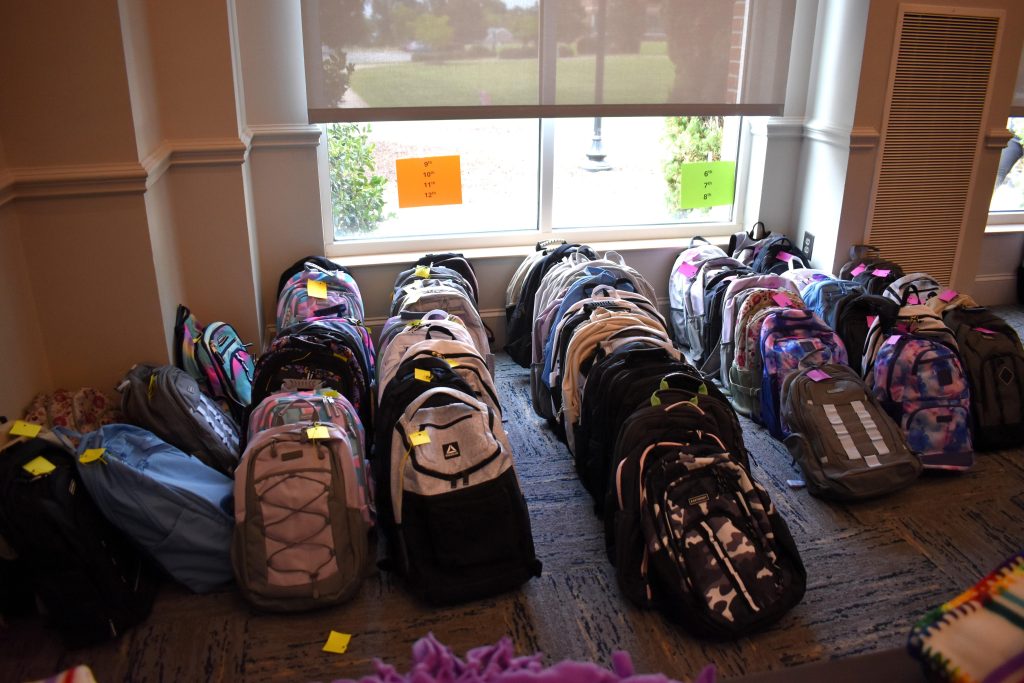 Seven rows of assorted book bags on the floor next to a window. Signage designates 9th - 12th grade and 6th - 8th grade.