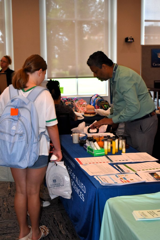 A man behind a table gives a presentation to a young girl. There are vials and food displays to teach nutrition.