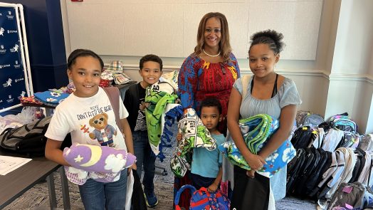 A woman poses with four younger children, they are all wearing backpacks and holding blankets