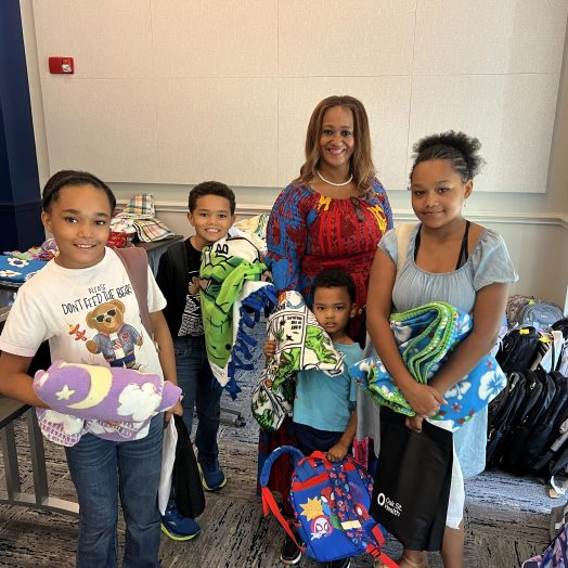 A woman poses with four younger children, they are all wearing backpacks and holding blankets