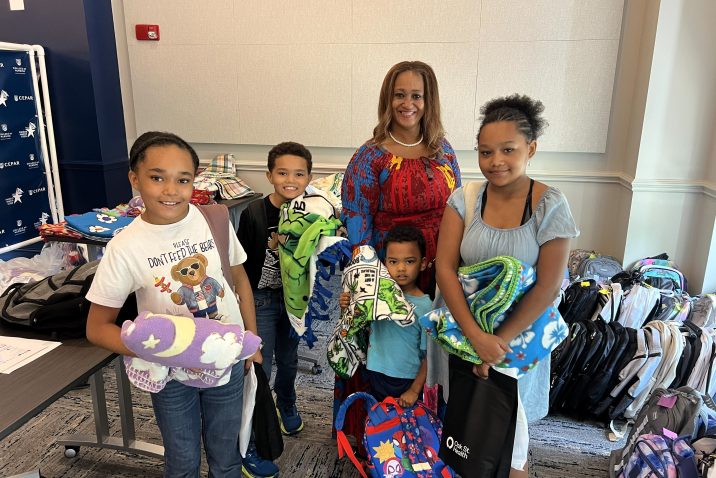 A woman poses with four younger children, they are all wearing backpacks and holding blankets
