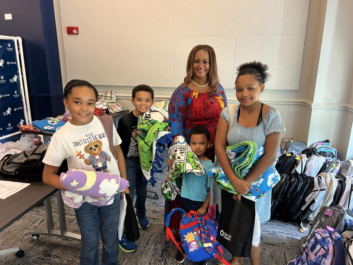 A woman poses with four younger children, they are all wearing backpacks and holding blankets